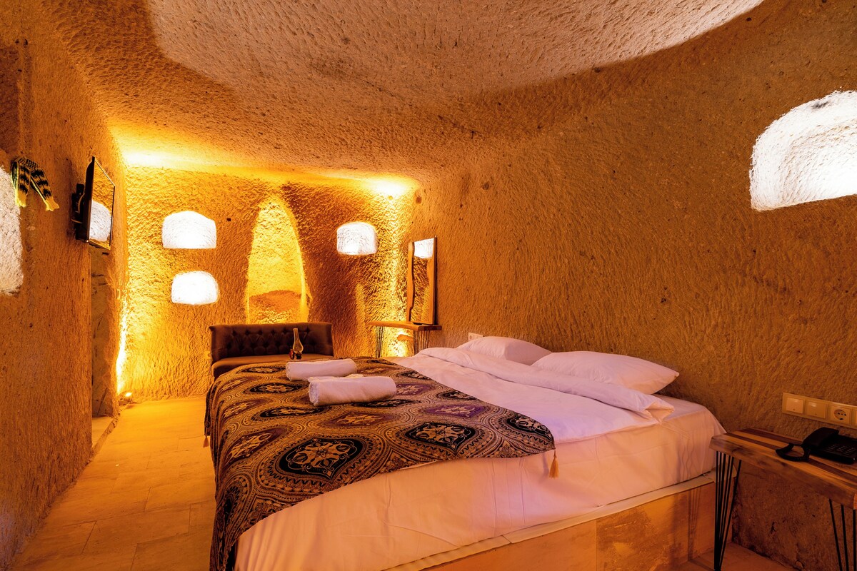 Un dormitorio acogedor con paredes de piedra, una cama grande, una mesita de noche de madera y un teléfono fijo en la pared.