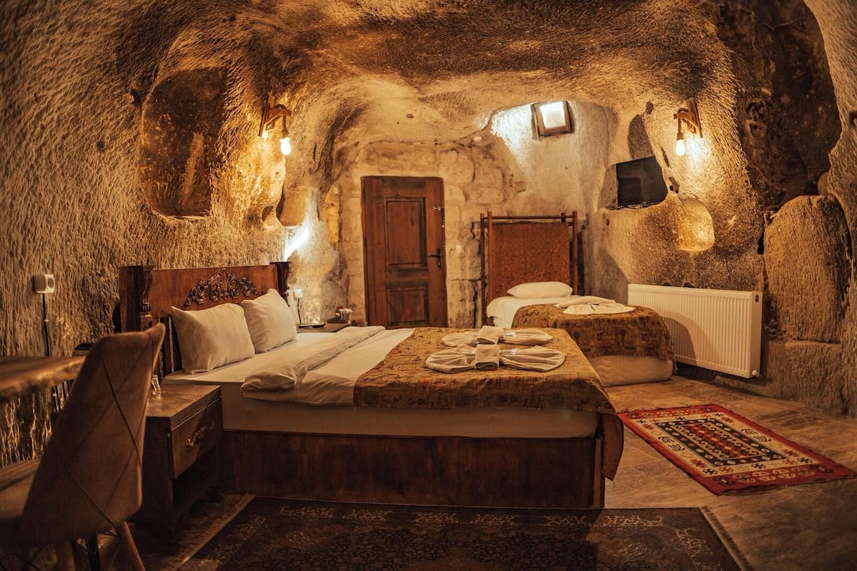 A cozy, rustic room with a large bed, a smaller bed, a wooden chair, a radiator, and a patterned rug.