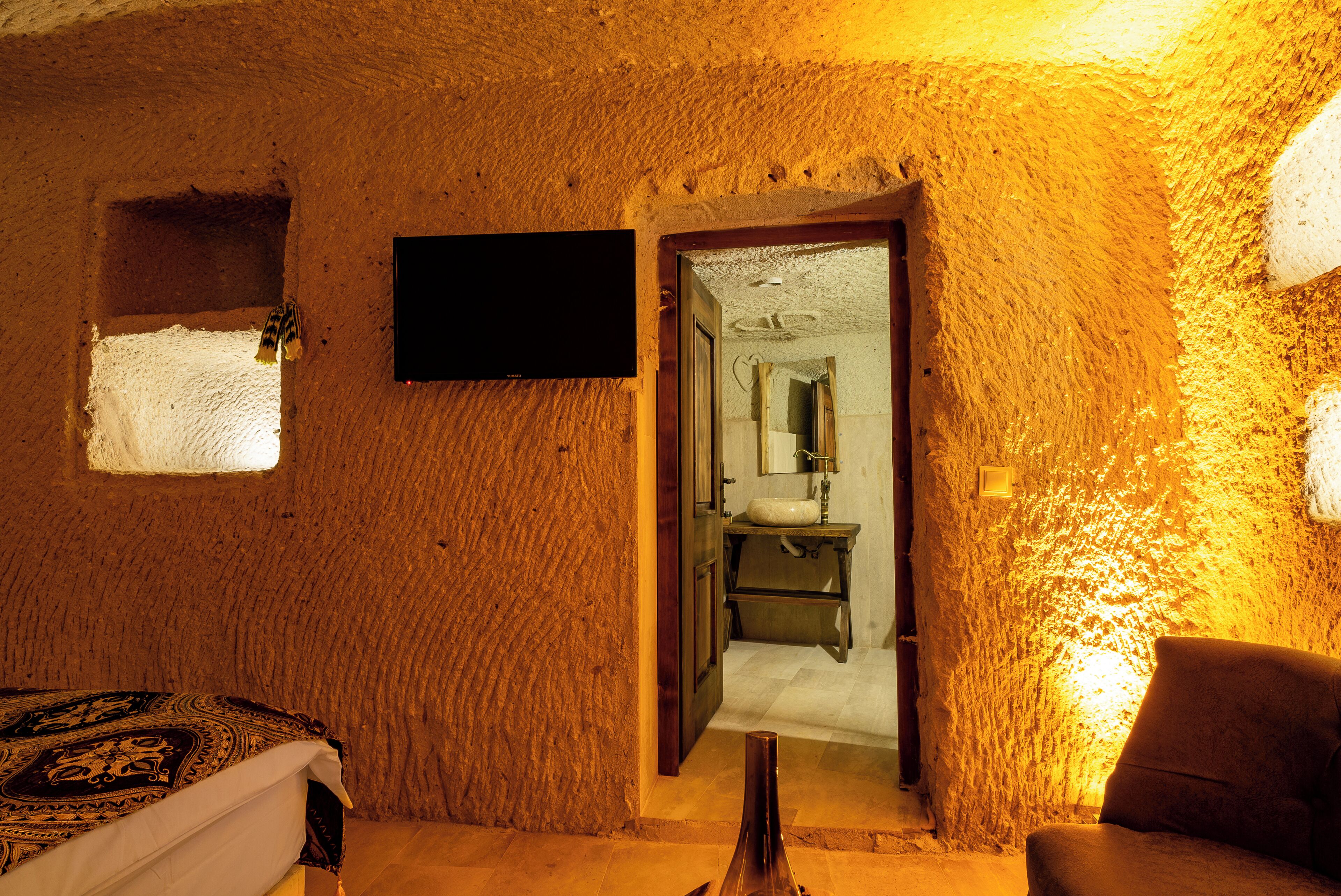 A room with a bed, a TV mounted on the wall, and a bathroom visible through an open door.