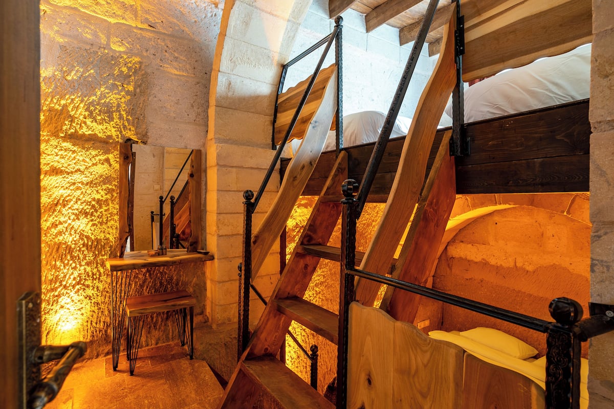 A rustic wooden staircase with a bench at the bottom, leading to a bed with a white pillow.
