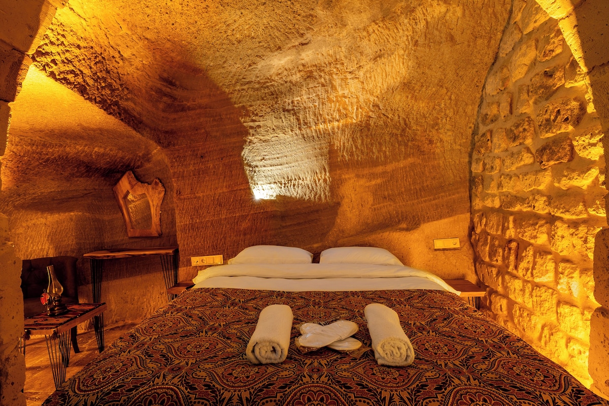 Un ambiente acogedor, parecido a una cueva, con una cama, una mesa de madera y una silla.