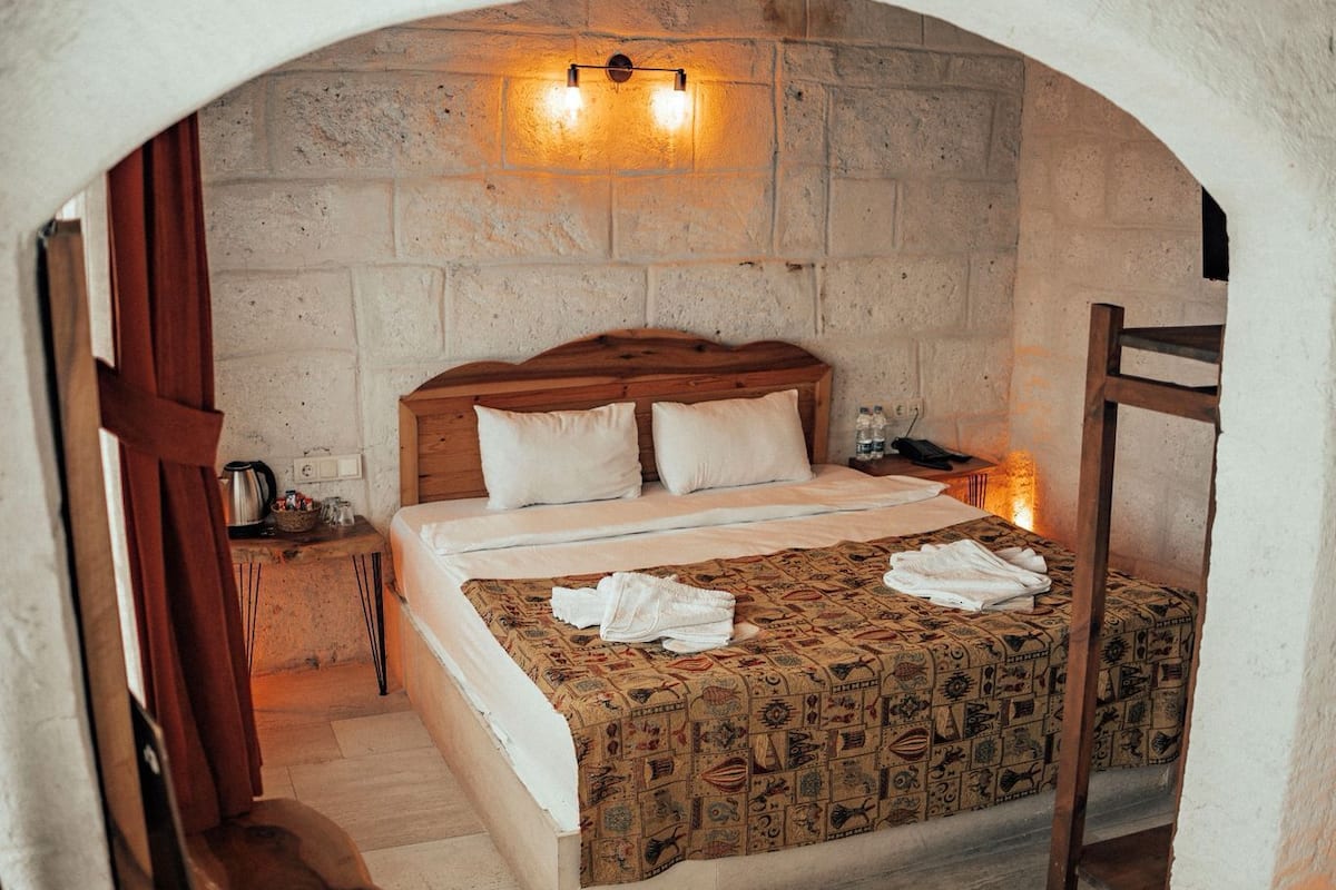 A bedroom with a wooden bed, a nightstand, a chair, and a stone wall.