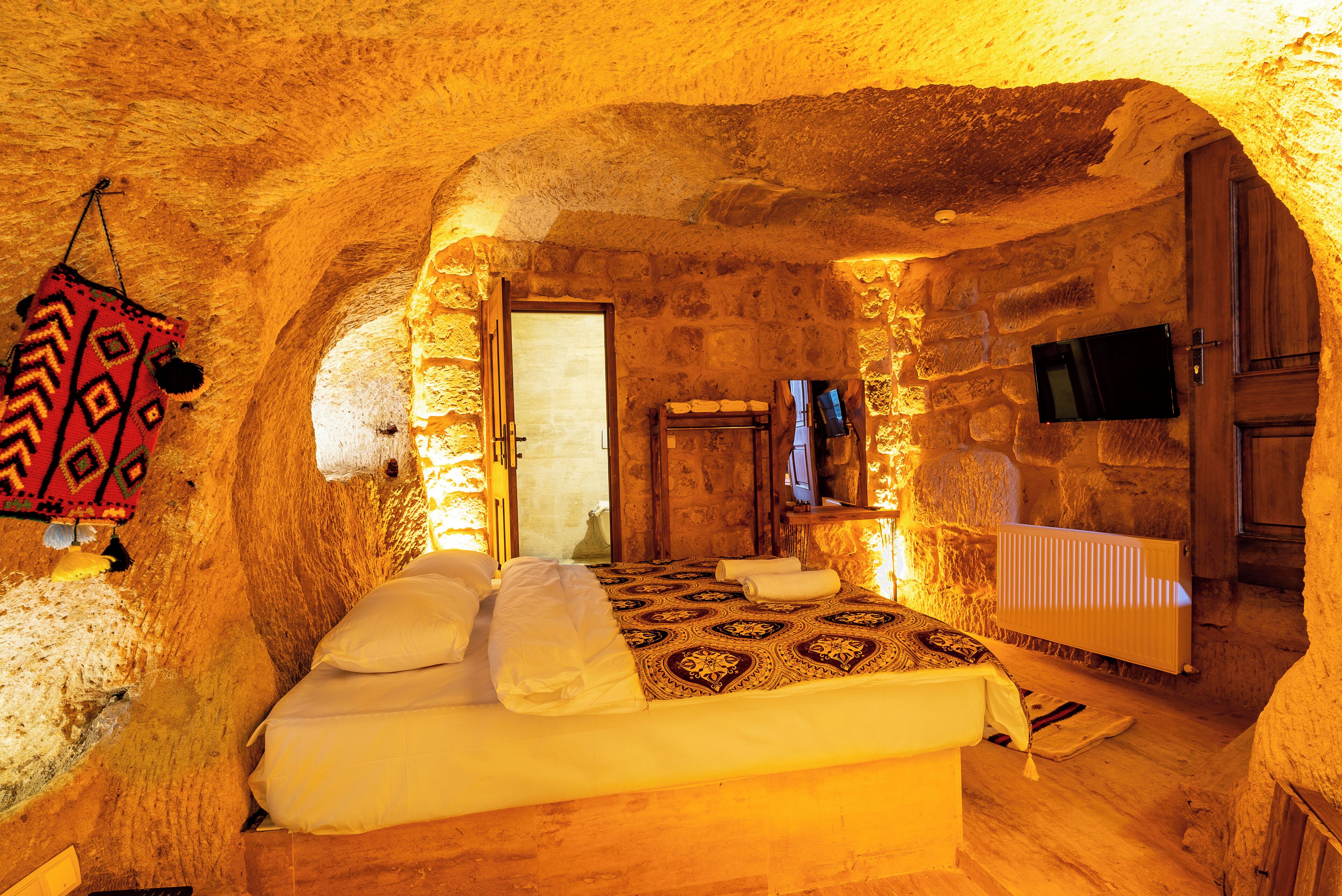 A cozy, stone-walled bedroom with a bed, a television, and a wooden door.