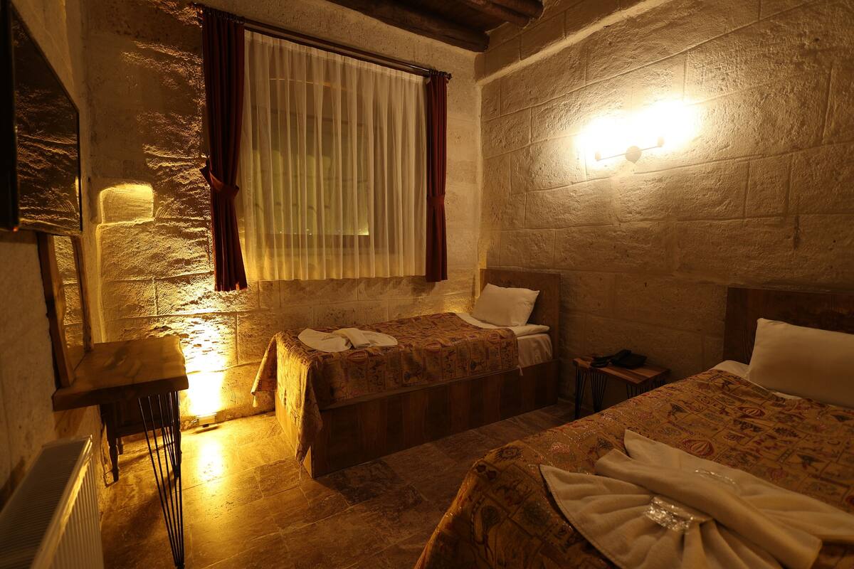 A room with two beds, a small table, and a window with curtains.