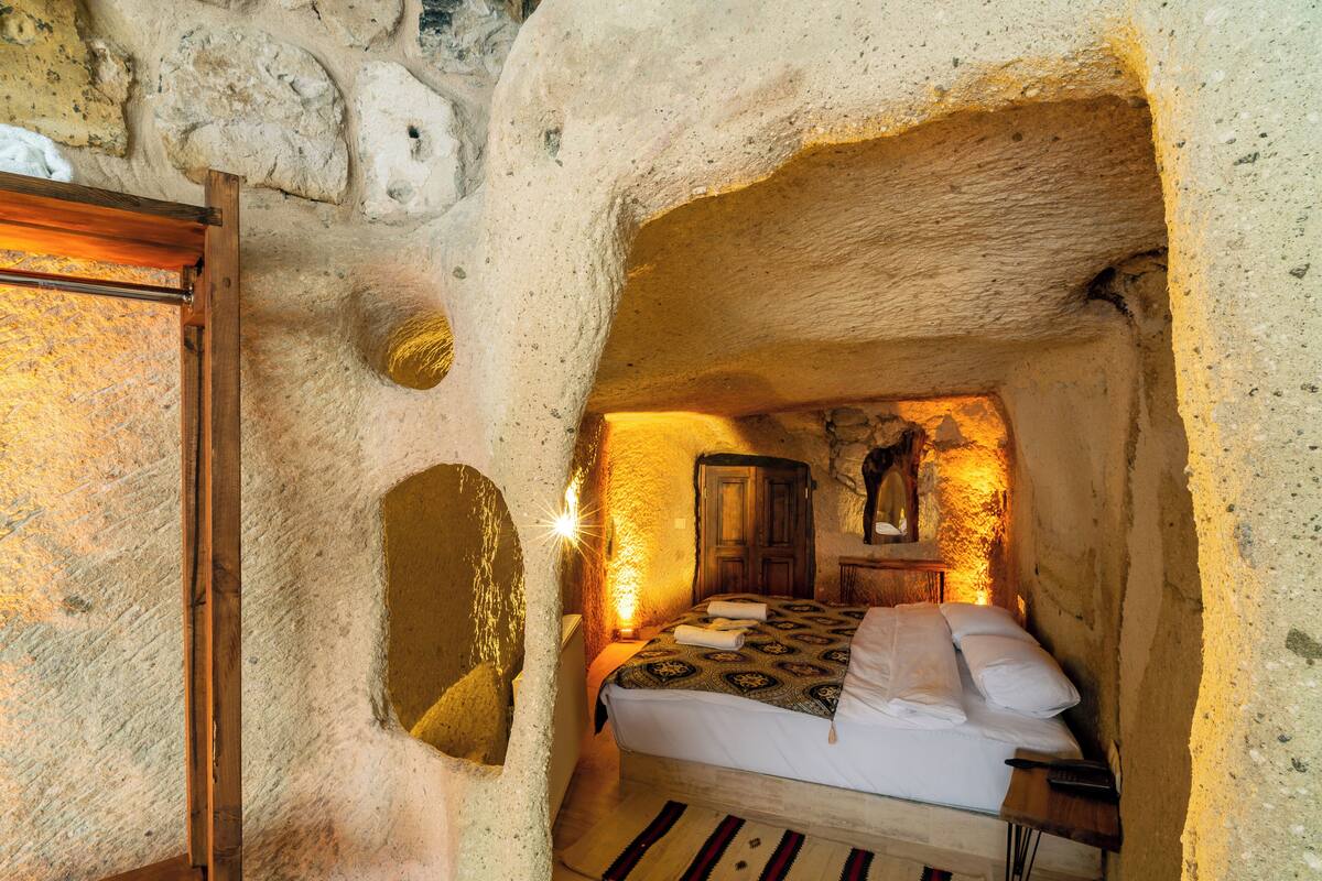 A cozy, cave-like bedroom with a bed, wooden furniture, and a stone wall.