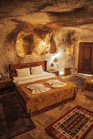 A room with a bed, a nightstand, a wooden door, and a patterned rug. - Snora Cave Hotel (Nevsehir)