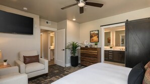 A bedroom with a bed, a chair, a dresser, a TV, and a bathroom visible through an open door. - Moab Sage Creek Arches Rest (Moab)