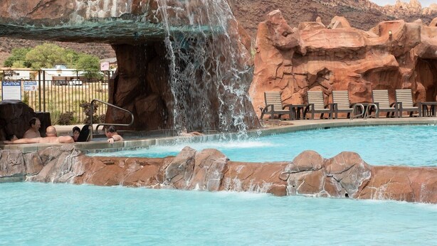 A pool with a waterfall feature, surrounded by rocky terrain and lounge chairs. - Moab Sage Creek Arches Rest (Moab)