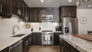 A modern kitchen with dark wood cabinets, stainless steel appliances, a granite countertop, and a tiled backsplash. - Moab Sage Creek Arches Rest (Moab)