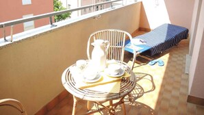 A balcony with a wicker chair, a small table with a pitcher, cups, and a tray, and a bed with a striped cover.