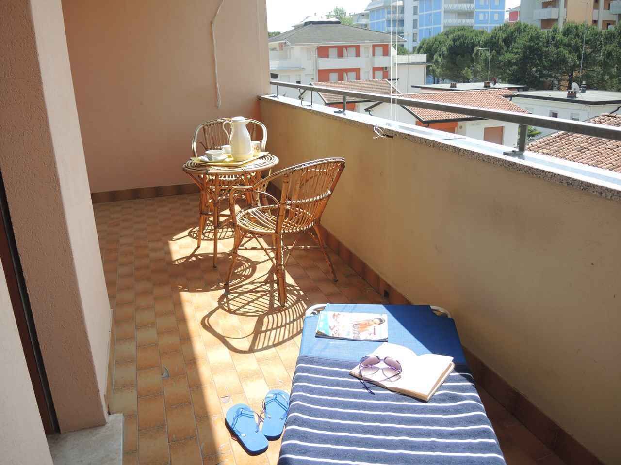 Uma varanda com mesa e cadeiras de vime, um sofá azul listrado e um par de chinelos azuis.