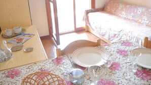 A room with a dining table set for two, a sofa, and a television on a cabinet.