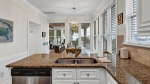 A kitchen with white cabinetry, a granite countertop, and a stainless steel dishwasher. - Sandy Toes | Iconic Oceanfront Home with Sunset Views at Grand Pavilion (Isle of Palms)
