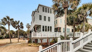 A multi-story building with a white exterior, a balcony, and a wooden deck with white railings. - Sandy Toes | Iconic Oceanfront Home with Sunset Views at Grand Pavilion (Isle of Palms)