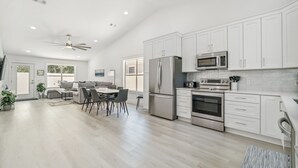 Una cucina moderna con mobili bianchi, elettrodomestici in acciaio inossidabile e un'area pranzo con tavolo e sedie.