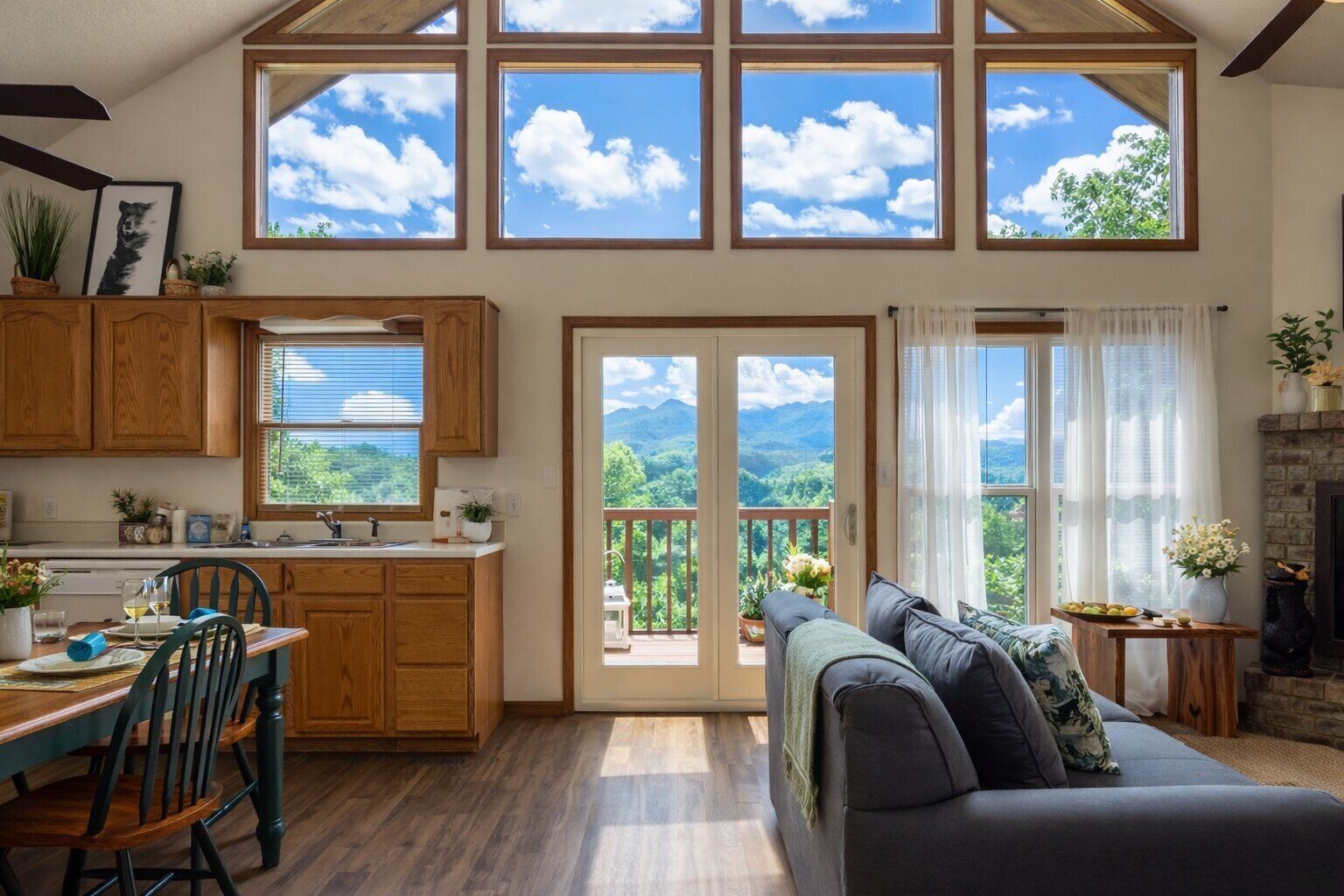 Un espacio habitable espacioso con un gran ventanal que da a un paisaje montañoso, un rincón de descanso acogedor con chimenea, y una cocina con armarios de madera y una mesa de comedor.