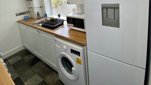 A compact kitchen with a washing machine, a microwave, and a refrigerator. - Gillingham cosy 3 bedroom with free WiFi & parking (Gillingham)