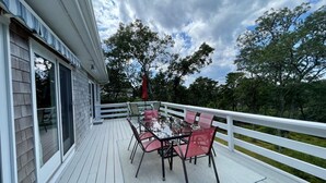 Une terrasse en bois avec une table et des chaises, une balustrade blanche et une vue sur les arbres et le ciel.
