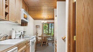 A kitchen with wooden cabinets, a microwave, a sink, and a dining area with chairs and a table.