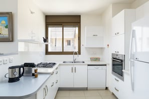 Uma cozinha moderna com armários brancos, fogão a gás, lava-louças e geladeira.