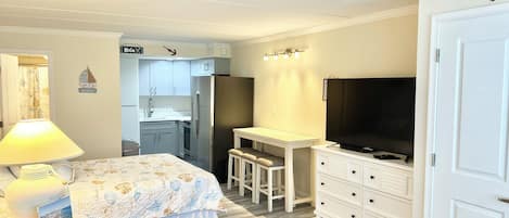 A compact bedroom with a bed, bedside lamp, a desk with a chair, a TV, and a wardrobe.