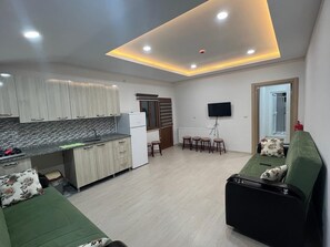 A modern kitchen with a built-in fridge, a dining area with a table and chairs, and a green sofa with floral cushions. - Uzungöl (Çaykara)
