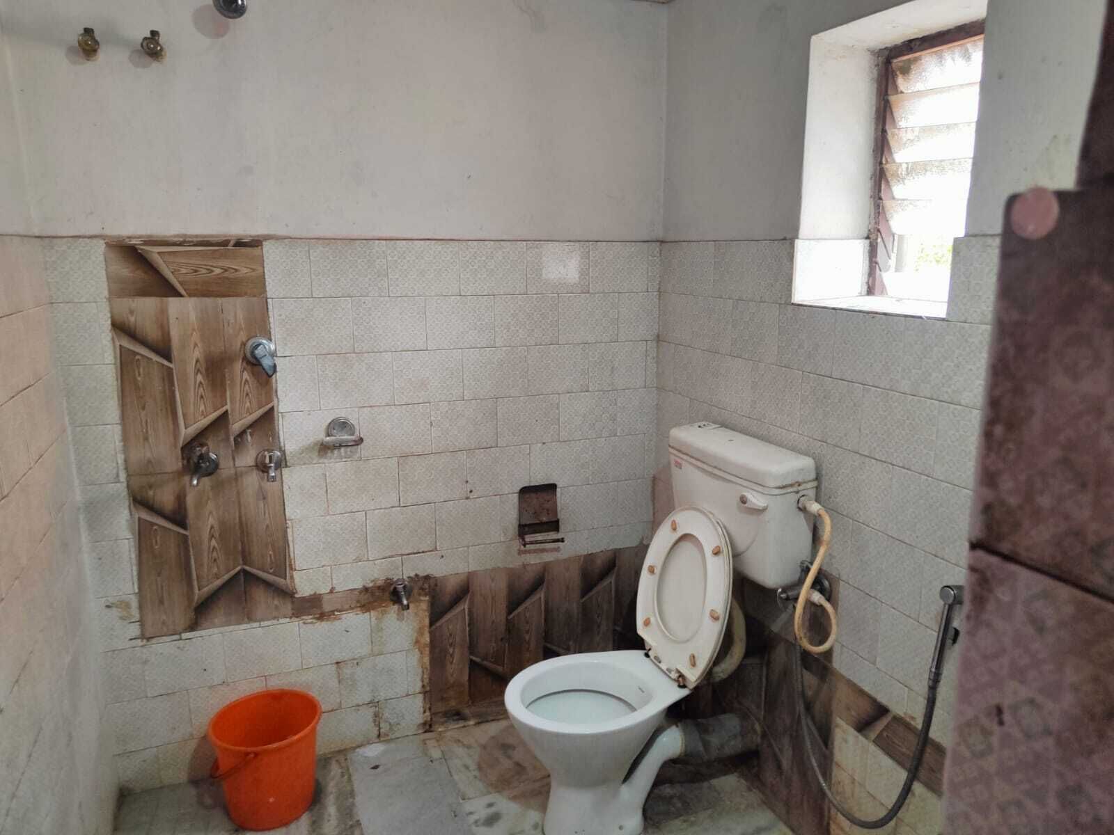 A small, basic bathroom with a toilet, a wooden shelf, and a window.