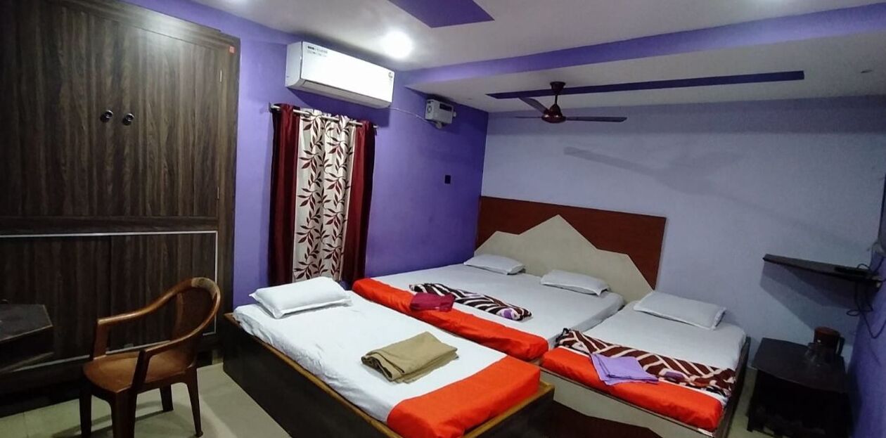 Quarto de hotel com duas camas, uma escrivaninha, uma cadeira e um ventilador de teto.