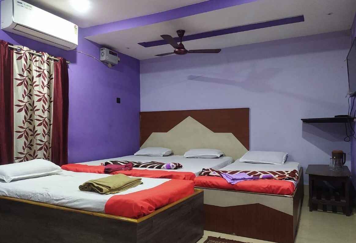 A room with two beds, a ceiling fan, an air conditioning unit, and a small table with a glass container.