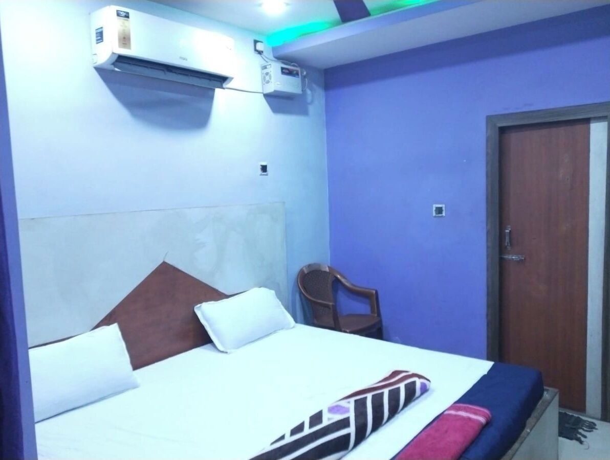 A hotel room with a bed, a chair, an air conditioning unit, and a door.