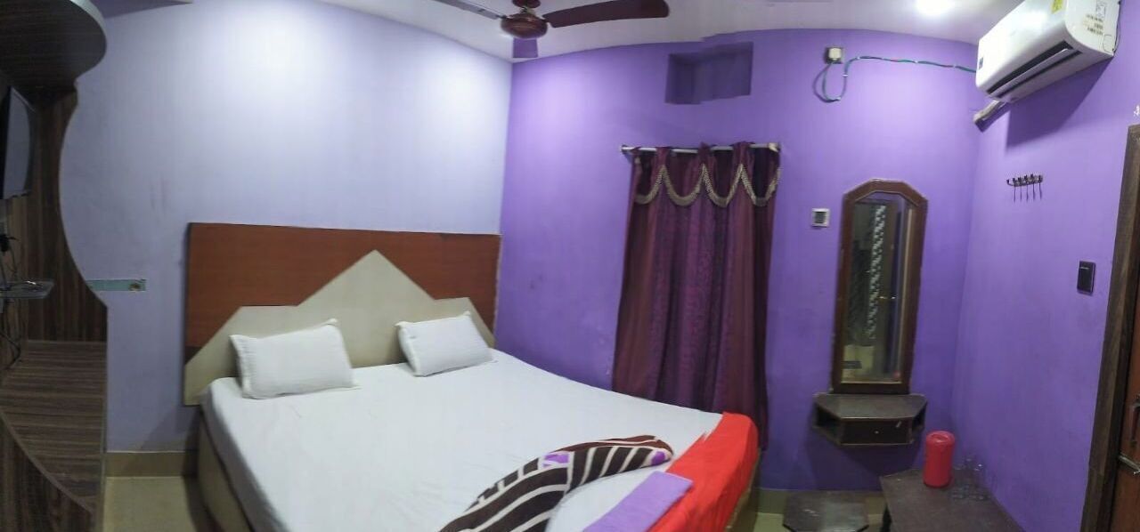 A bedroom with a bed, a ceiling fan, an air conditioning unit, a mirror, and a window with curtains.