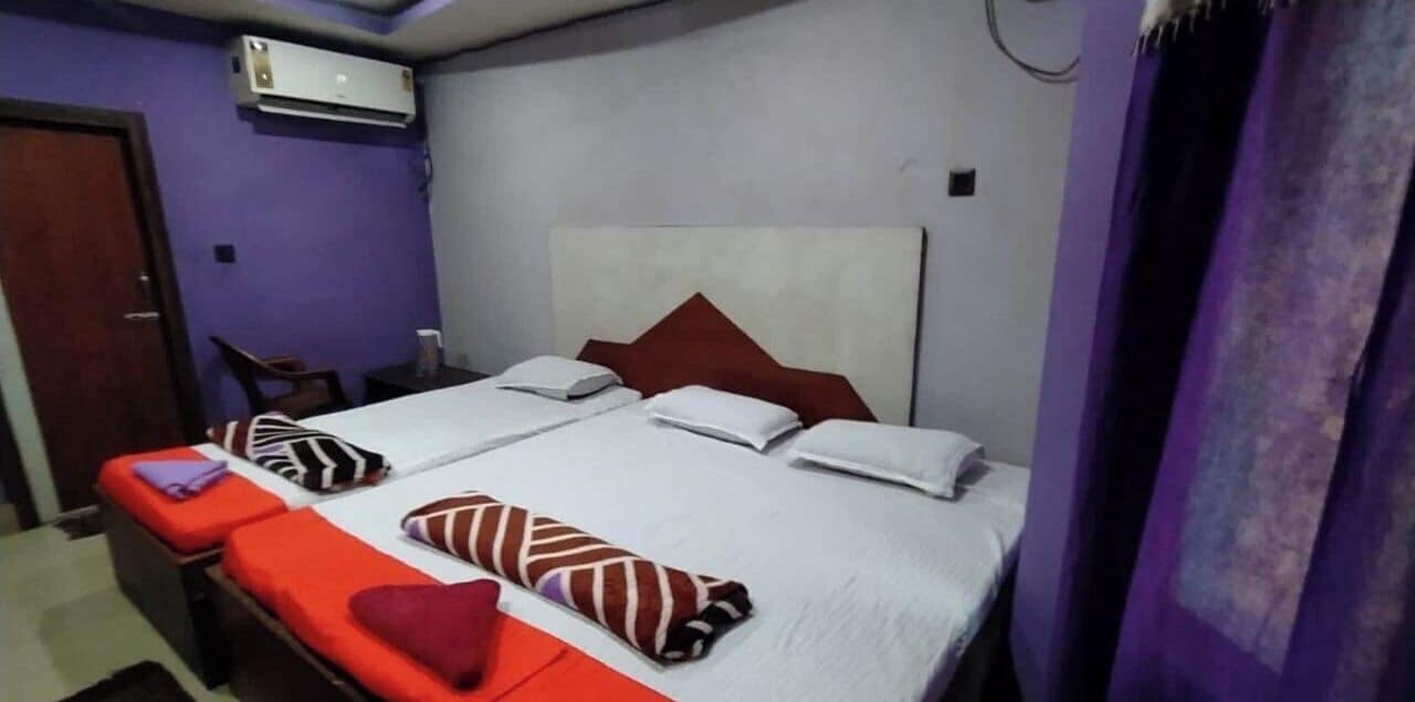 A double bed with white linens and red and white pillows, a small bedside table, and a chair.
