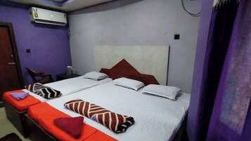 Una cama doble con sábanas blancas y almohadas rojas y blancas, una mesita de noche pequeña y una silla.