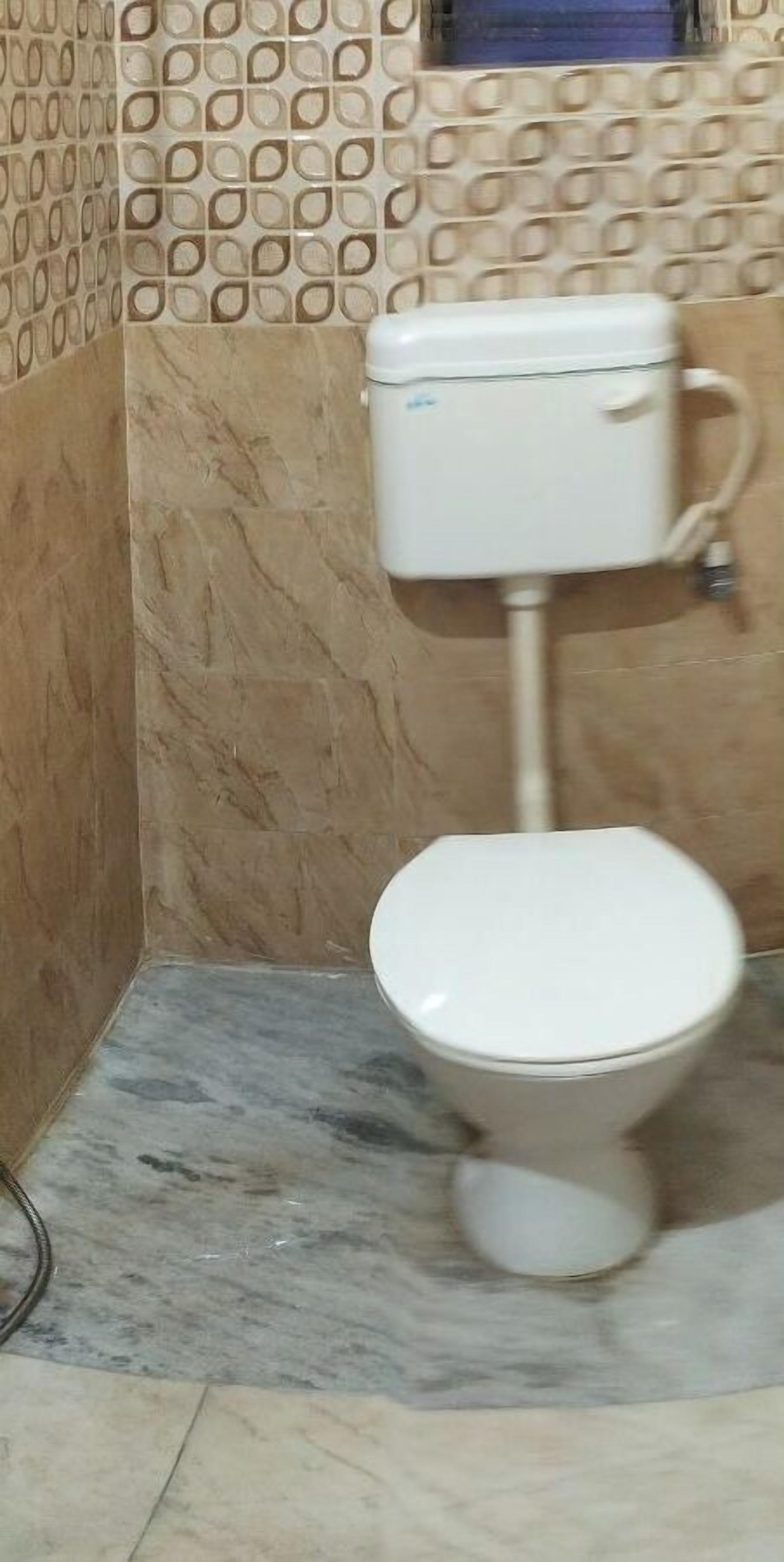 A bathroom with a toilet, a marble floor, and a patterned wall.