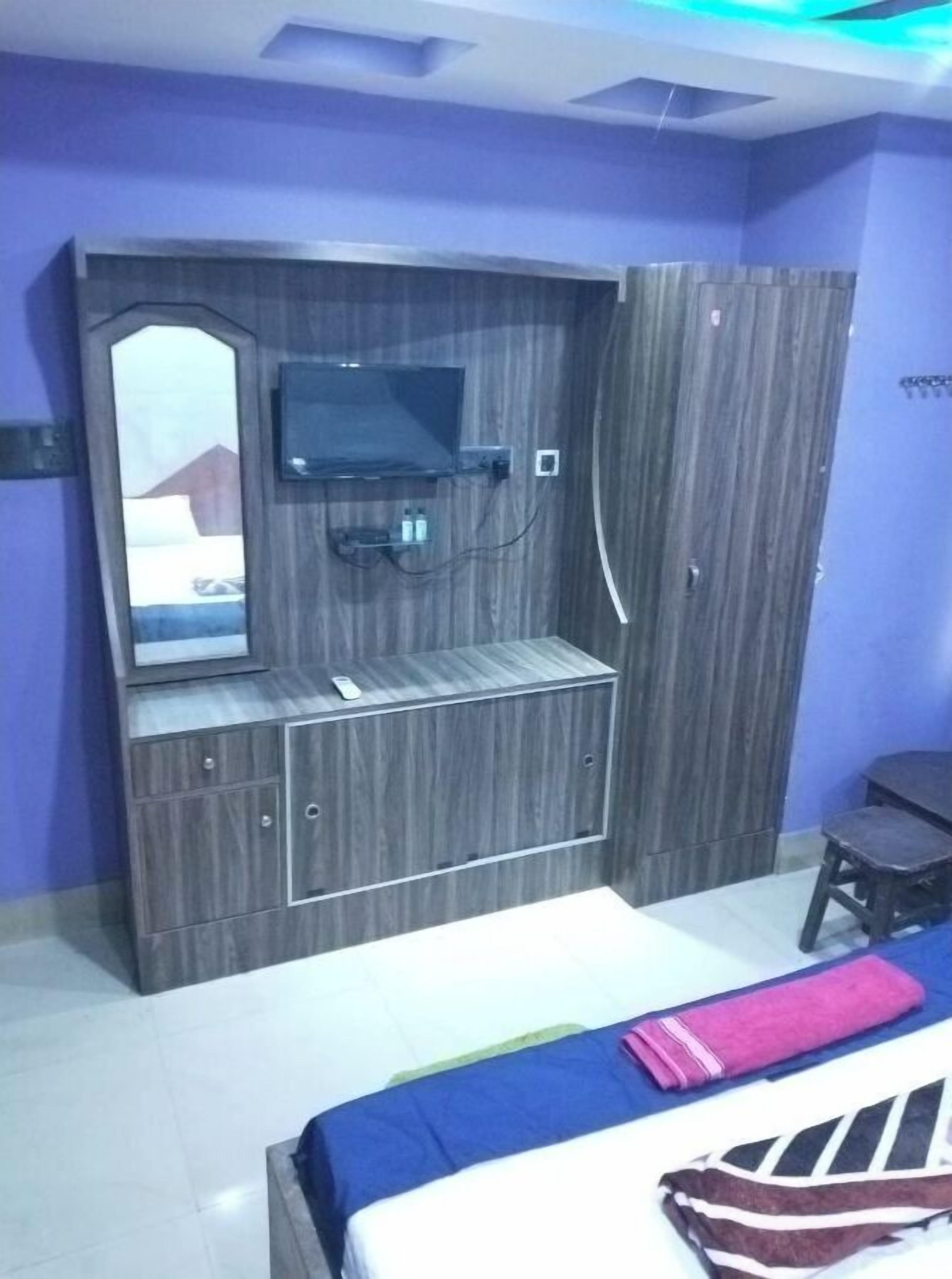 A bedroom with a bed, a TV mounted on a wooden cabinet, and a small desk.