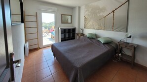 A bedroom with a bed, a nightstand, a desk, a chair, a wardrobe, a door, and a view of the outside. - Appartement "rooftop" Avec Très Grande Terrasse à 2km de la mer (Roquebrune-sur-Argens)