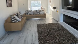 Un salon moderne avec un canapé beige, un grand téléviseur à écran plat et un tapis à motifs.