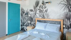 Une chambre avec un plafond de couleur turquoise, un lit recouvert de draps blancs, une fresque murale représentant des plantes tropicales et une porte en bois.