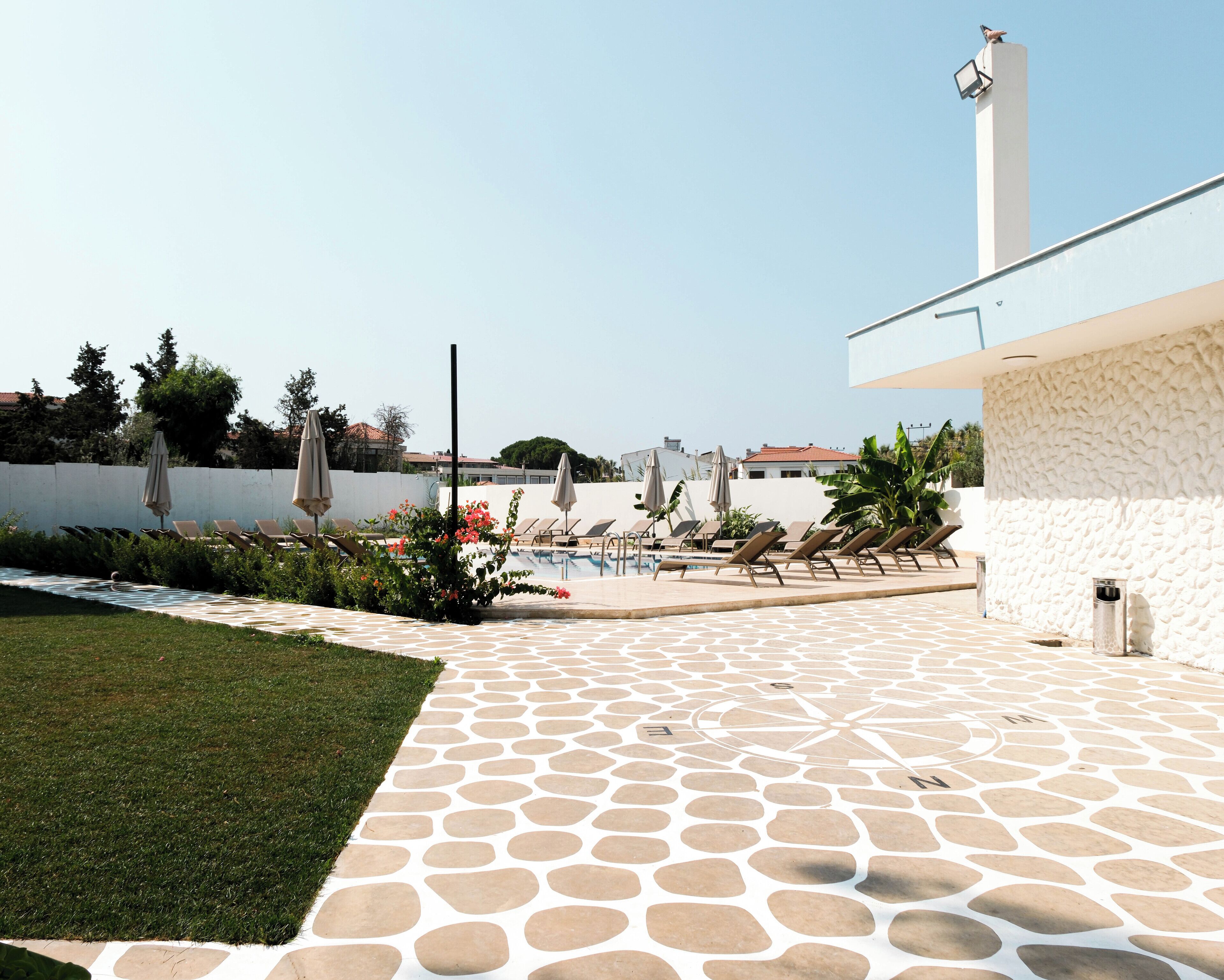 Un área junto a la piscina con sillones de descanso y sombrillas, suelo de piedra estampada y vista despejada de los edificios circundantes.