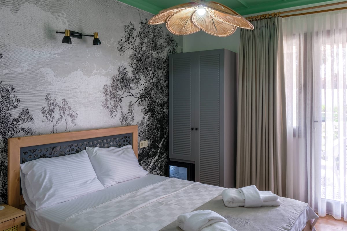 A neatly made bed with white linens, a hanging lamp, and a wardrobe in a room with green walls and a patterned wallpaper.