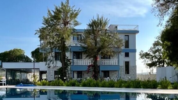 Un hôtel moderne doté d’une piscine, dont l’eau reflète le bâtiment et les arbres environnants.