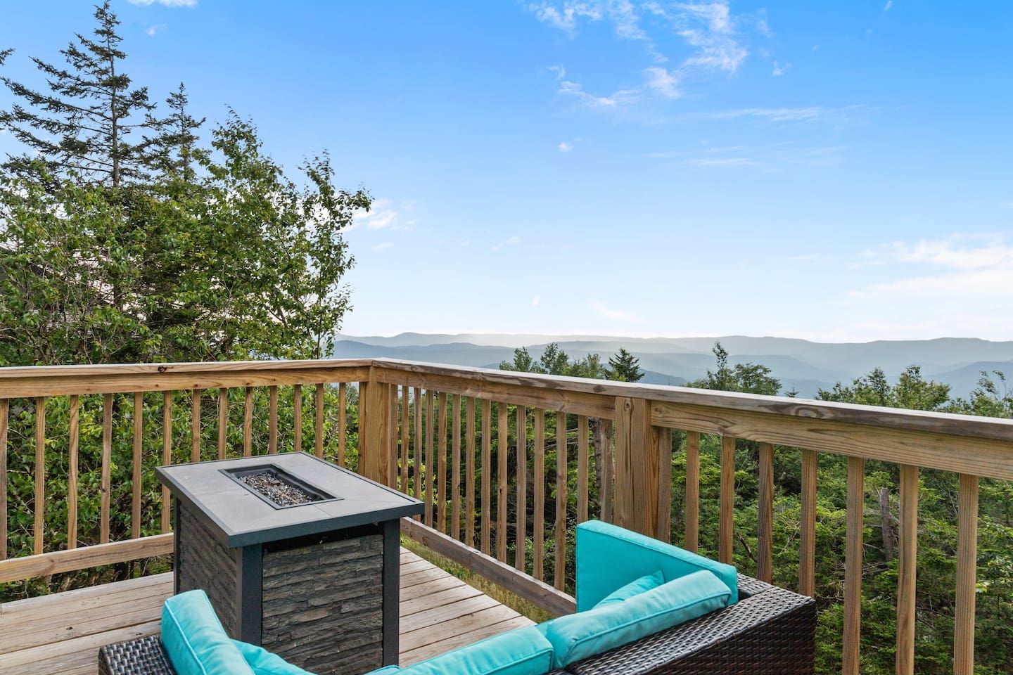 A wooden deck with a stone fireplace, turquoise cushions, and a view of distant mountains.