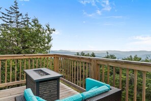 A wooden deck with a stone fireplace, turquoise cushions, and a view of distant mountains. - Hutch 1- 2 Min Walk to Slopes, Great Mountain View (Slaty Fork)