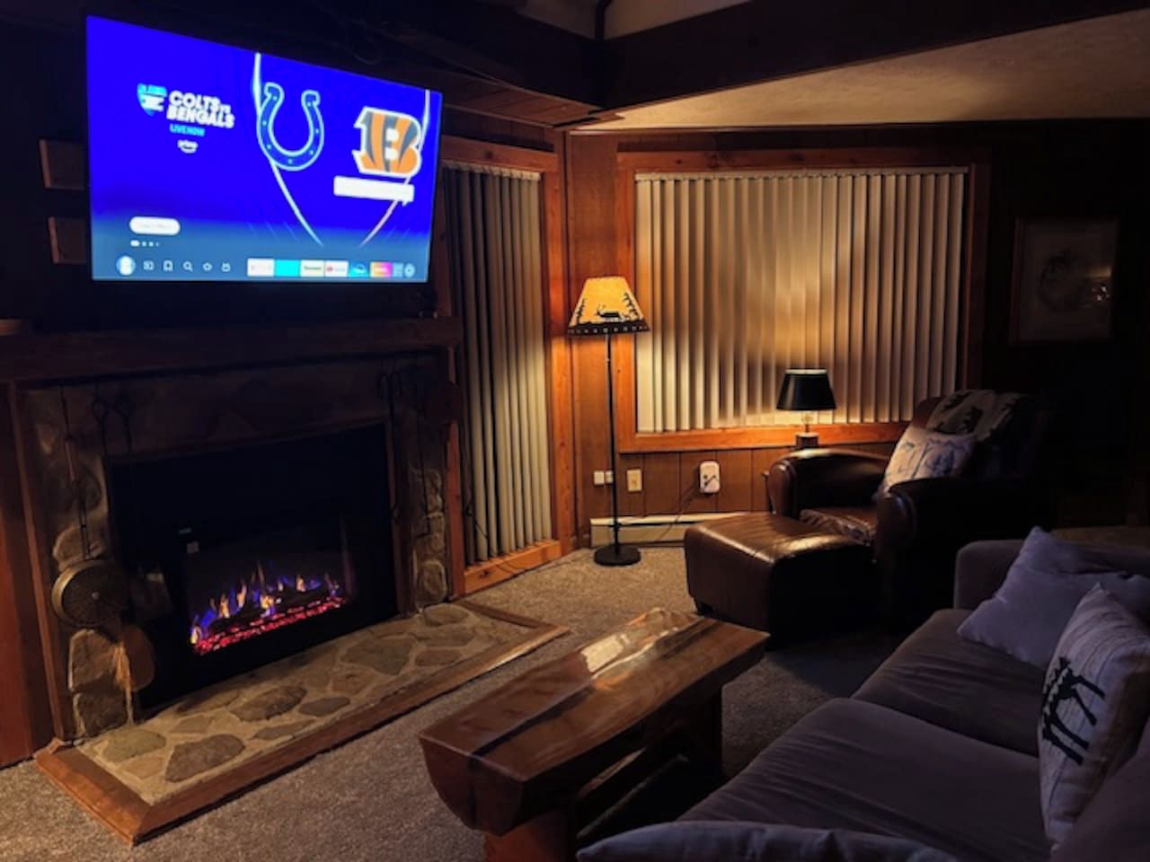Ein Wohnzimmer mit Kamin aus Stein, einem Flachbildfernseher, einer Couch, einem Couchtisch und einer Lampe.