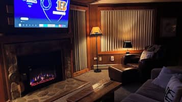 Ein Wohnzimmer mit Kamin aus Stein, einem Flachbildfernseher, einer Couch, einem Couchtisch und einer Lampe.