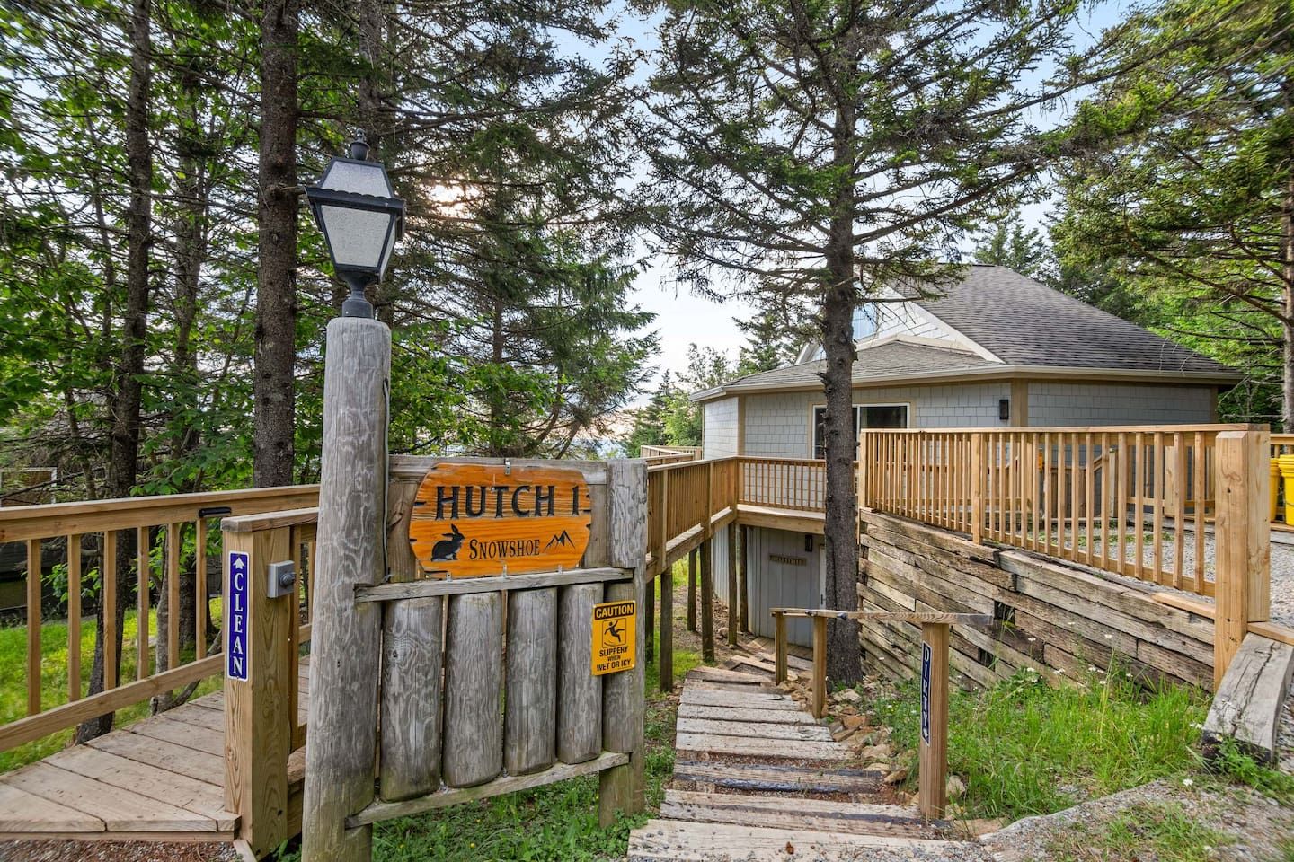 A wooden staircase leading to a cabin labeled 'Hutch 1 Snowshoe' with a caution sign for slippery steps.