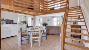 Un salón amplio con una escalera de madera, una mesa de comedor con sillas y una cocina al fondo.