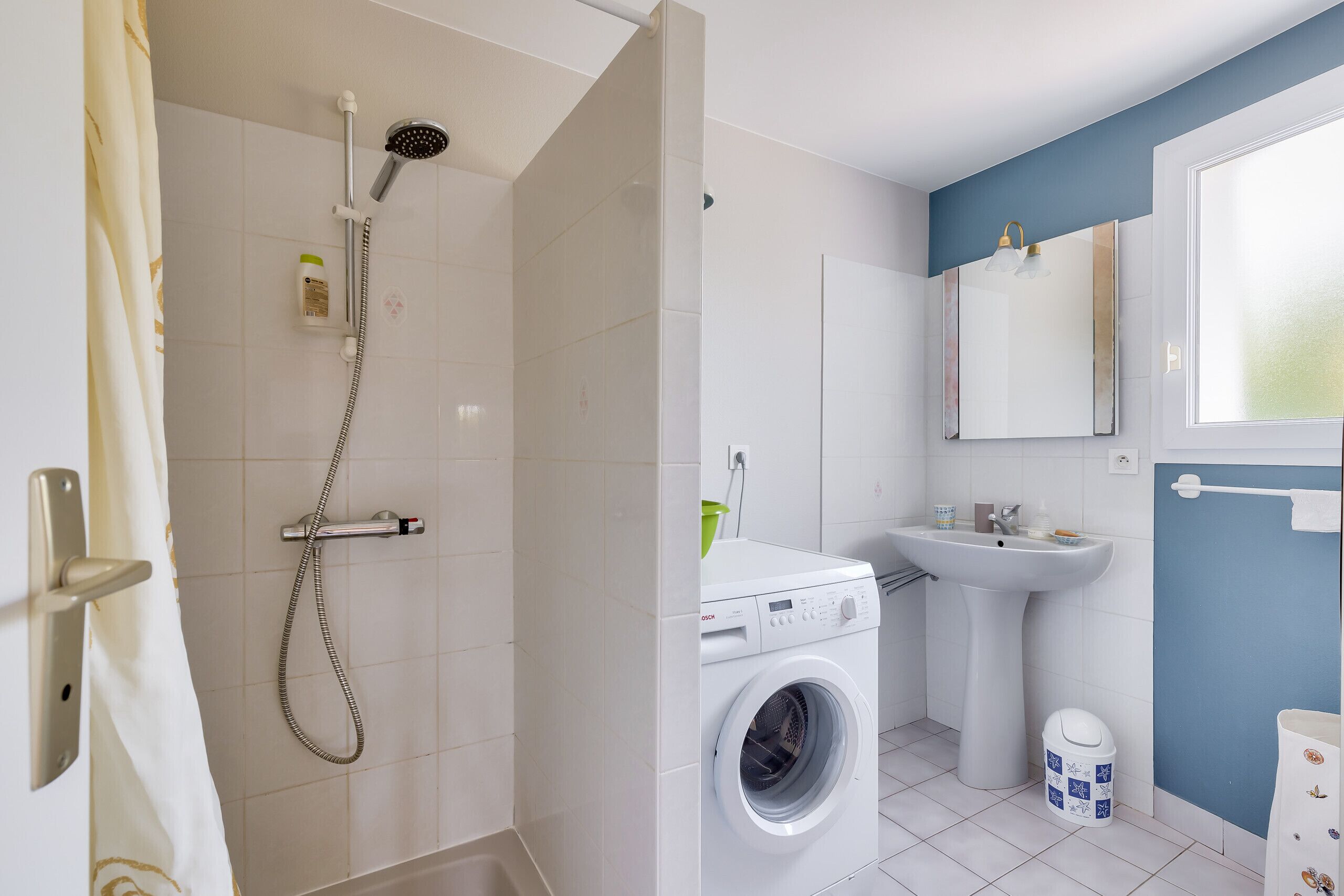 Badeværelse med bruser, vaskemaskine, håndvask og toilet.