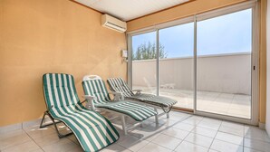 A sunroom with three striped lounge chairs, a sliding glass door to a balcony, and an air conditioning unit on the wall. - 200m from the sea, 6 adults and 4 children (La Plaine-sur-Mer)