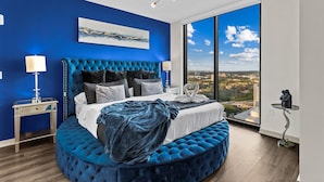 A bedroom with a large bed, a view of a cityscape, and a modern chandelier.